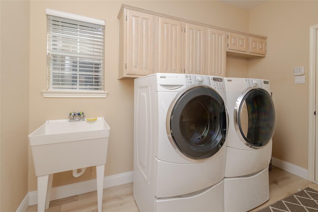 washroom with light wood-type flooring, cabinet space, baseboards, and washing machine and dryer