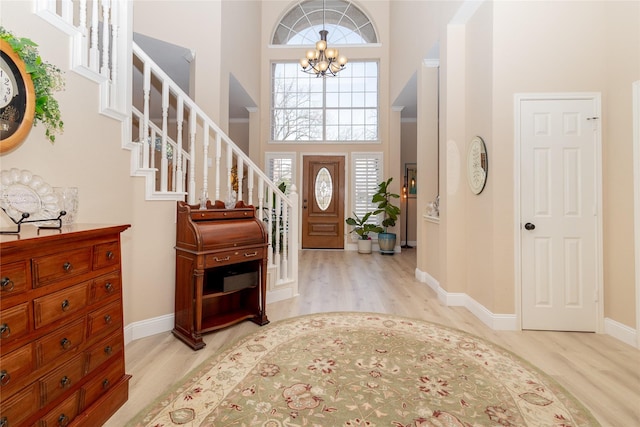 foyer with wood finished floors, stairway, a high ceiling, an inviting chandelier, and baseboards