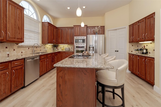 kitchen featuring a kitchen bar, a sink, a kitchen island, light wood-style floors, and appliances with stainless steel finishes