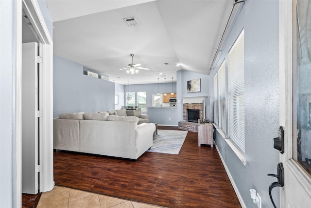 living room with wood finished floors, a ceiling fan, visible vents, lofted ceiling, and a brick fireplace