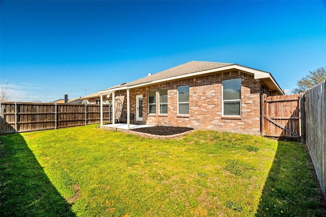 rear view of house featuring brick siding, a fenced backyard, a yard, a patio area, and a gate