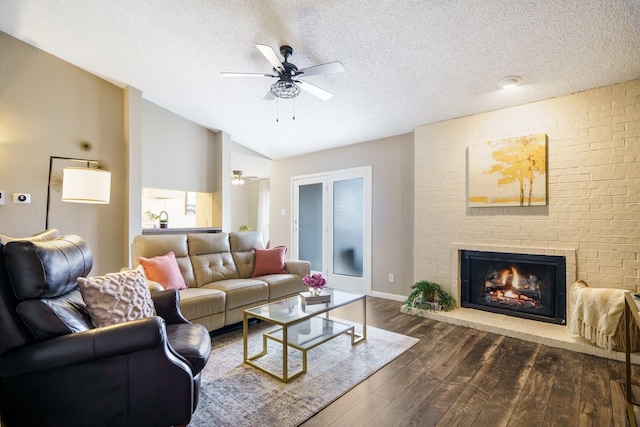 living area with dark wood finished floors, vaulted ceiling, a fireplace, a textured ceiling, and a ceiling fan