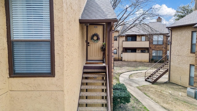 entrance to property featuring stucco siding and roof with shingles