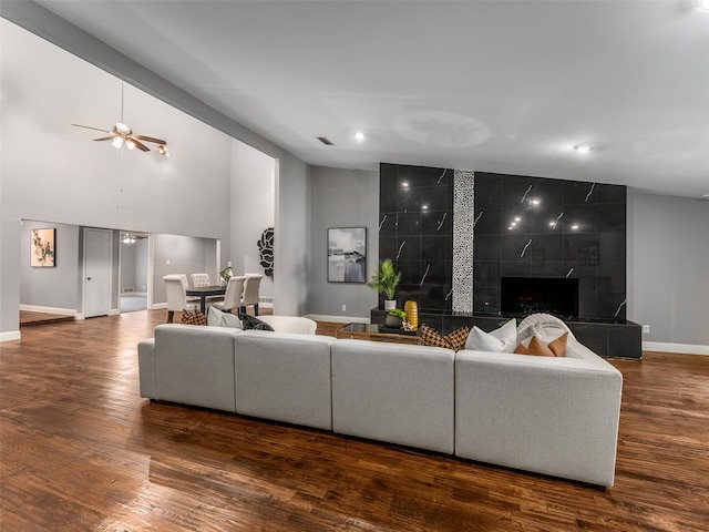 living area featuring wood finished floors, baseboards, high vaulted ceiling, ceiling fan, and a tile fireplace