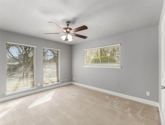 unfurnished room with a wealth of natural light, visible vents, light colored carpet, and ceiling fan