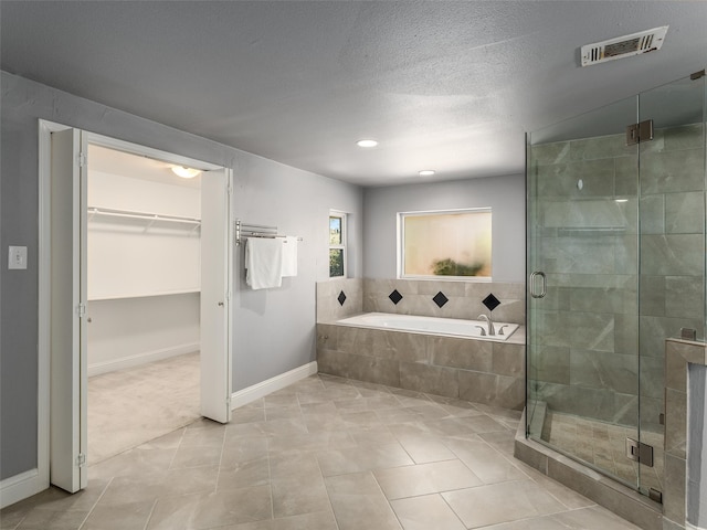 full bath featuring visible vents, a shower stall, a walk in closet, a garden tub, and a textured ceiling