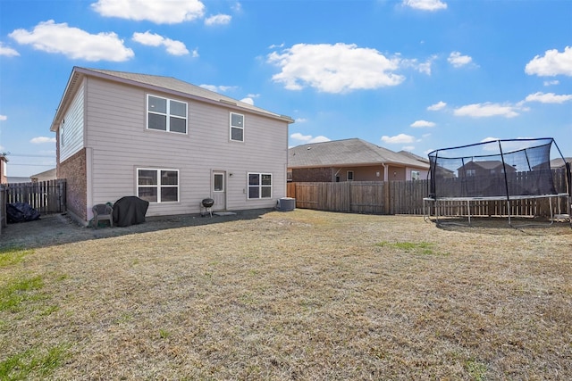 rear view of property with a fenced backyard, a lawn, brick siding, and a trampoline