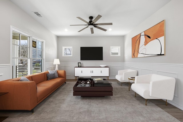 living area featuring a ceiling fan, a healthy amount of sunlight, a decorative wall, and visible vents