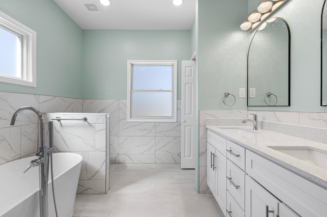 bathroom featuring a sink, visible vents, double vanity, and a freestanding tub