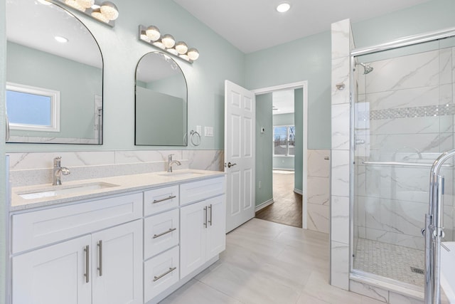 full bath featuring double vanity, a marble finish shower, and a sink