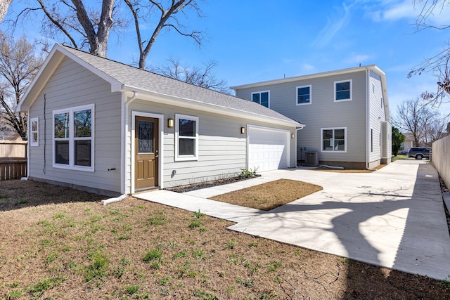 back of house featuring fence, driveway, roof with shingles, an attached garage, and central air condition unit