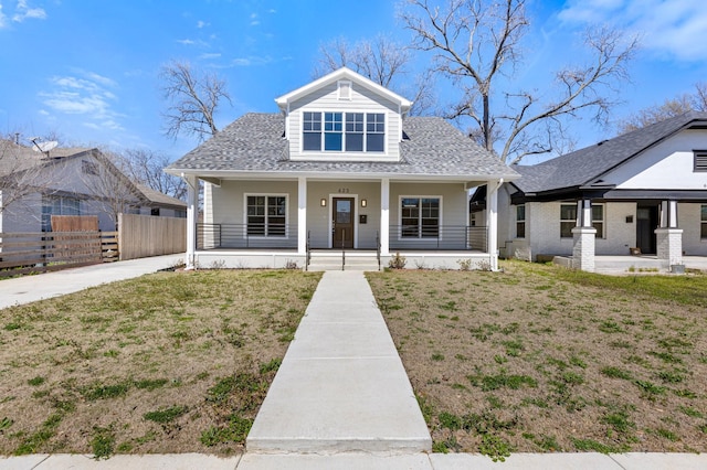 view of front facade featuring a porch, a shingled roof, a front lawn, and fence