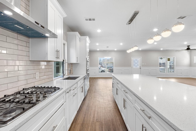 kitchen featuring visible vents, stainless steel gas cooktop, a sink, white cabinets, and wall chimney exhaust hood