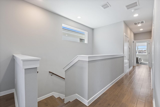 corridor featuring wood finished floors, an upstairs landing, baseboards, and visible vents