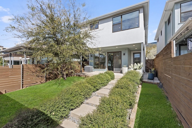 rear view of property with central AC unit, fence, and a lawn