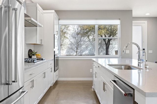 kitchen featuring a sink, appliances with stainless steel finishes, wall chimney exhaust hood, decorative backsplash, and baseboards