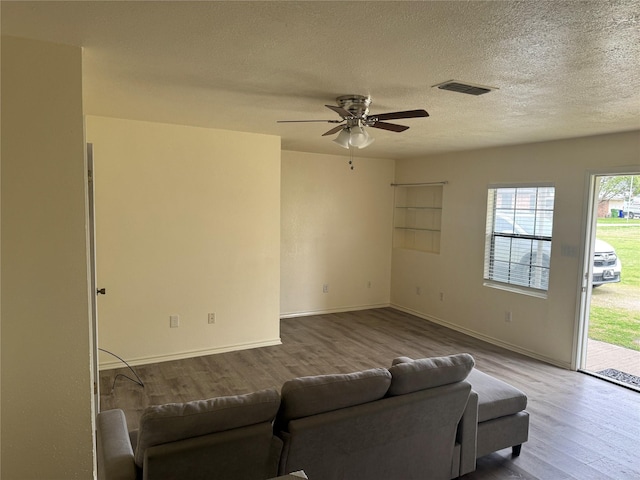 living room with visible vents, a textured ceiling, wood finished floors, baseboards, and ceiling fan