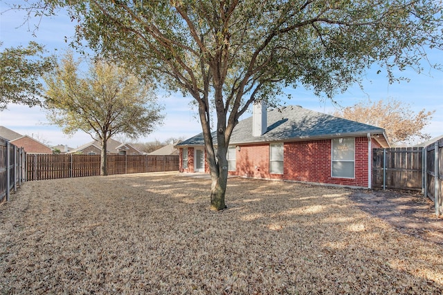 rear view of house with roof with shingles, a fenced backyard, a chimney, a lawn, and brick siding