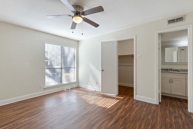 unfurnished bedroom featuring a sink, visible vents, dark wood-type flooring, and a spacious closet