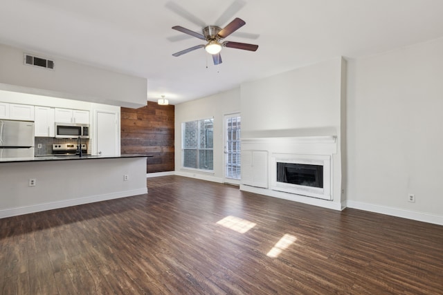 unfurnished living room with visible vents, a ceiling fan, dark wood-style floors, a fireplace, and baseboards