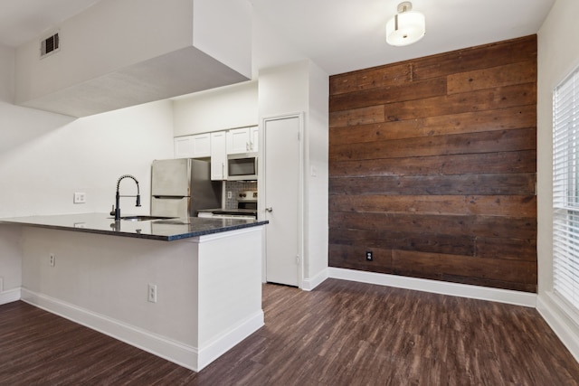 kitchen featuring visible vents, appliances with stainless steel finishes, a peninsula, dark wood-style floors, and a sink