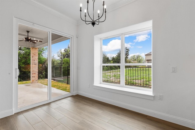 unfurnished dining area featuring ornamental molding, ceiling fan with notable chandelier, baseboards, and wood finished floors