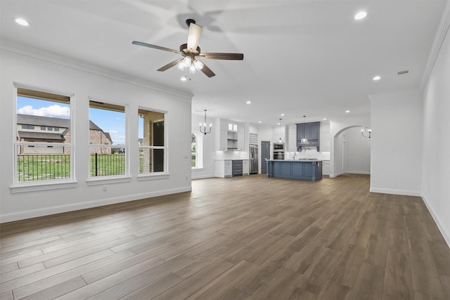 unfurnished living room with ceiling fan with notable chandelier, crown molding, dark wood-style floors, and baseboards