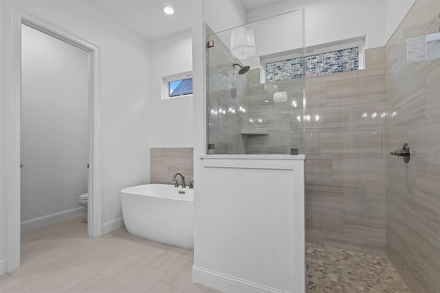 bathroom with a soaking tub, toilet, a walk in shower, and baseboards