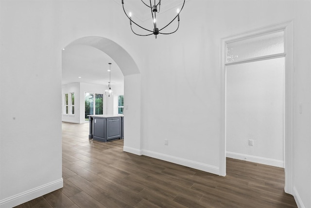 unfurnished room featuring baseboards, arched walkways, an inviting chandelier, and dark wood-style floors