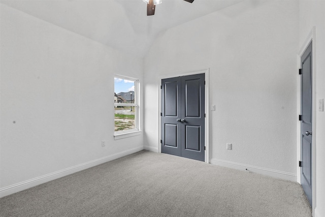 empty room featuring vaulted ceiling, carpet flooring, a ceiling fan, and baseboards