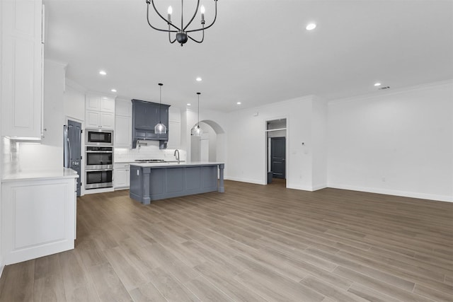 kitchen featuring arched walkways, light countertops, appliances with stainless steel finishes, a notable chandelier, and backsplash