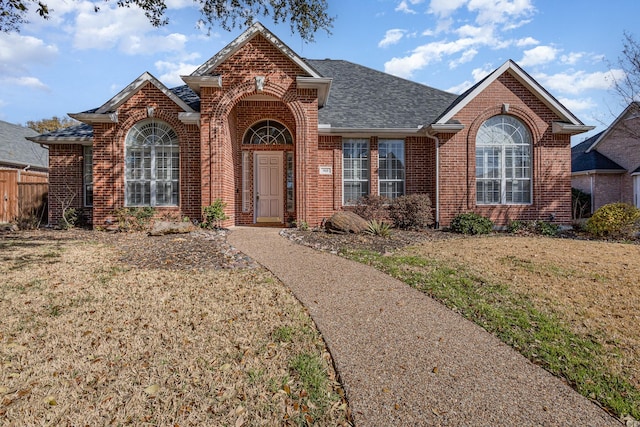 view of front of home with a front lawn, fence, brick siding, and roof with shingles