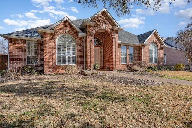 view of front of property with brick siding, a front lawn, and roof with shingles