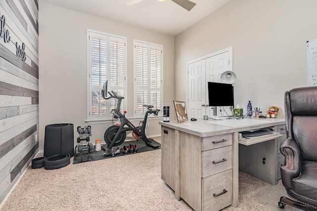 office featuring a ceiling fan, light colored carpet, and wood walls