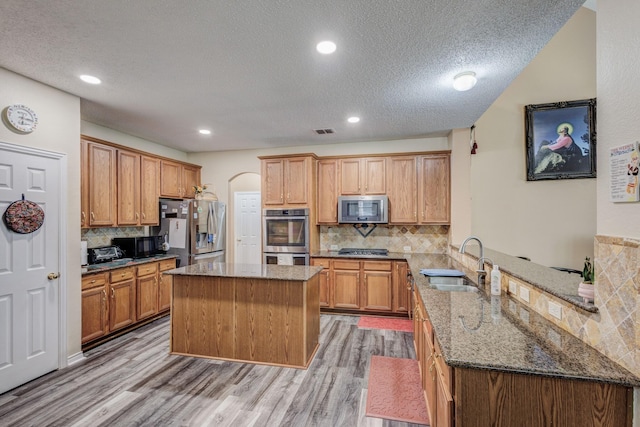 kitchen featuring a sink, dark stone counters, arched walkways, appliances with stainless steel finishes, and a peninsula