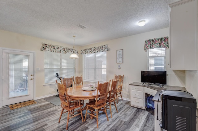 dining room featuring light wood-type flooring, visible vents, baseboards, and a textured ceiling