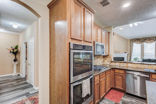 kitchen with visible vents, arched walkways, stainless steel appliances, decorative backsplash, and light wood-style floors