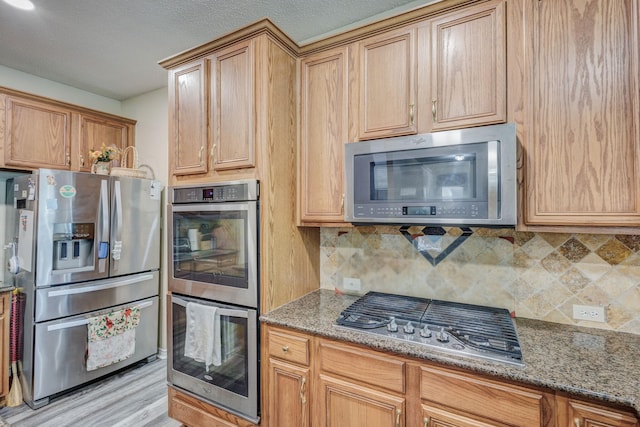 kitchen with light stone counters, backsplash, a textured ceiling, light wood-style floors, and appliances with stainless steel finishes