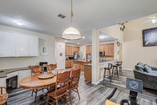 dining space with visible vents, baseboards, light wood-style floors, a textured ceiling, and a ceiling fan