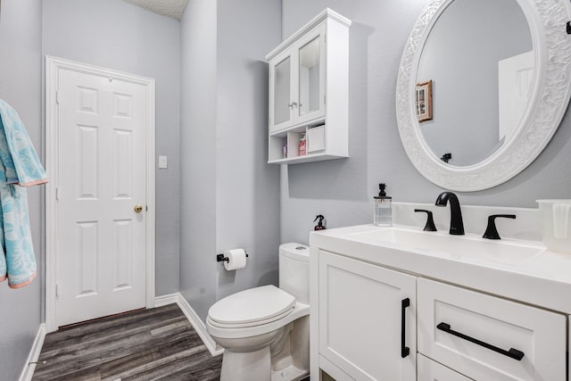 bathroom featuring baseboards, toilet, wood finished floors, and vanity