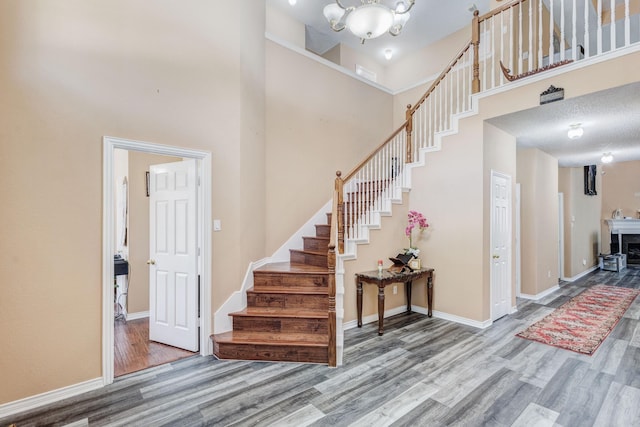 staircase with visible vents, baseboards, wood finished floors, a towering ceiling, and an inviting chandelier