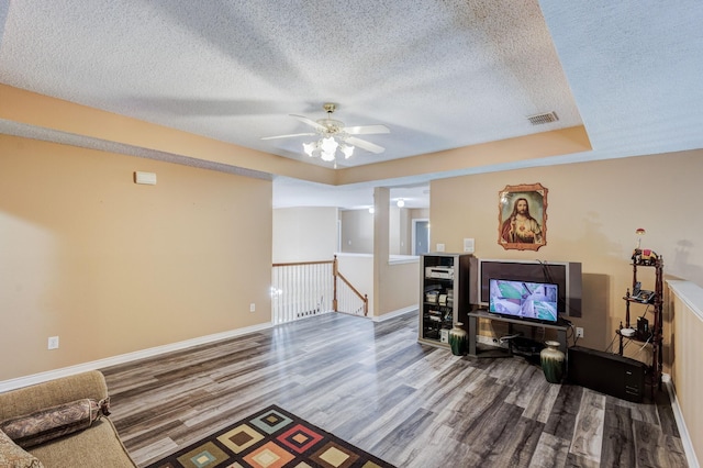 living area featuring a ceiling fan, baseboards, wood finished floors, visible vents, and a textured ceiling