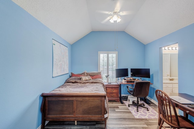 bedroom featuring lofted ceiling, ensuite bathroom, light wood-style floors, baseboards, and ceiling fan