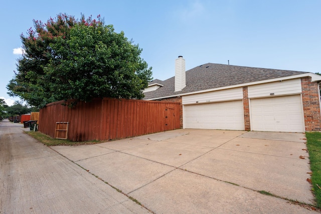 exterior space featuring fence, roof with shingles, concrete driveway, an attached garage, and brick siding