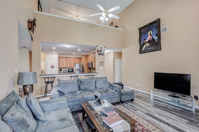 living room featuring wood finished floors, baseboards, visible vents, a high ceiling, and ceiling fan