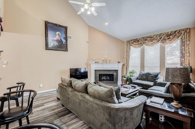 living area featuring baseboards, ceiling fan, a fireplace, wood finished floors, and high vaulted ceiling