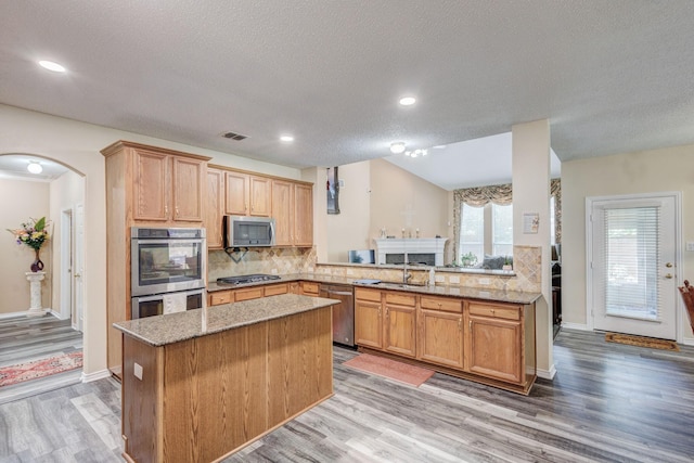 kitchen with light stone counters, a kitchen island, arched walkways, stainless steel appliances, and decorative backsplash