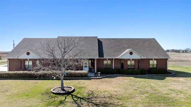 view of front of home featuring a front yard, brick siding, and roof with shingles