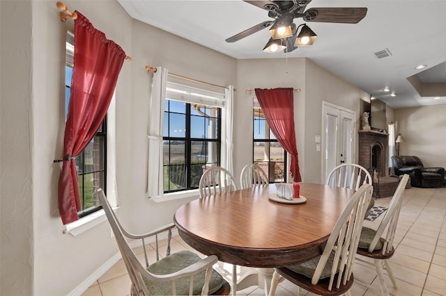 dining space featuring visible vents, a fireplace, light tile patterned floors, baseboards, and ceiling fan