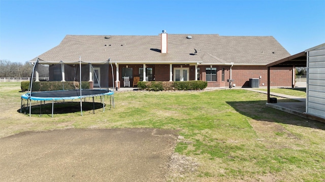 back of property featuring brick siding, a trampoline, central air condition unit, a chimney, and a yard